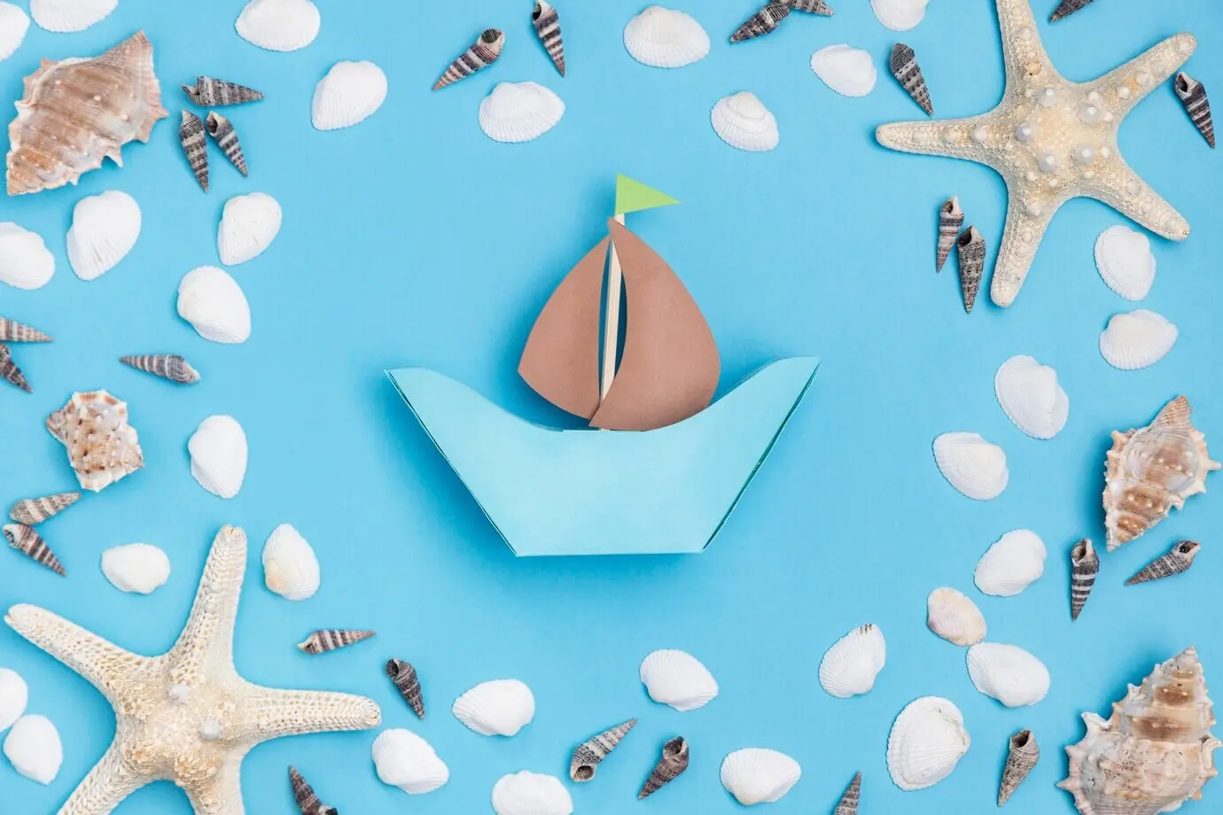Вид сверху на бумажную лодку с морской звездой и морскими ракушками.