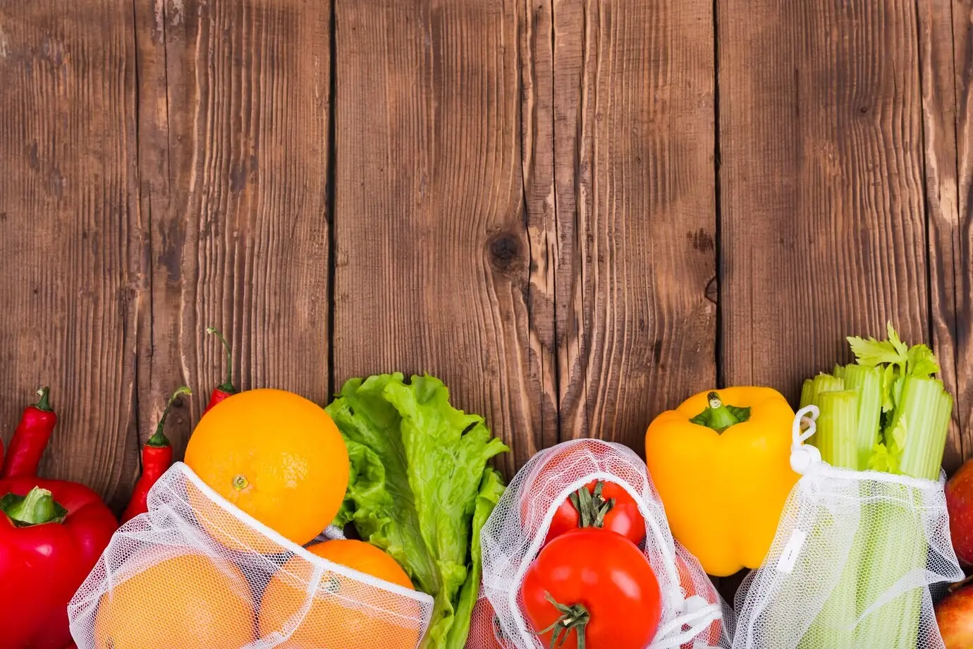 Вид сверху на многоразовые сумки с овощами и фруктами на деревянной поверхности.